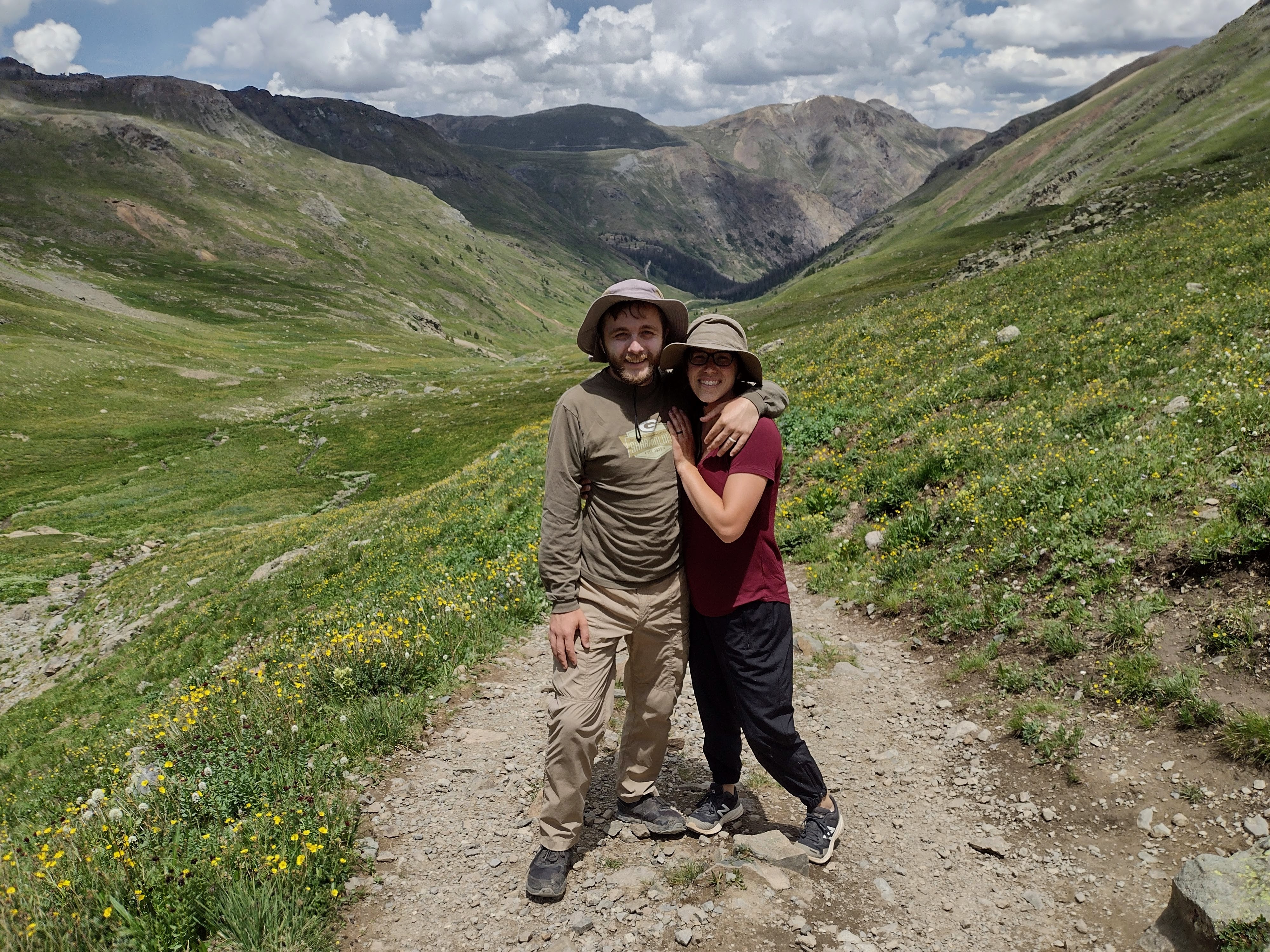 My wife Julia and I stand in front of the flowering American Basin, with bare mountains and thunderclouds in the distance
